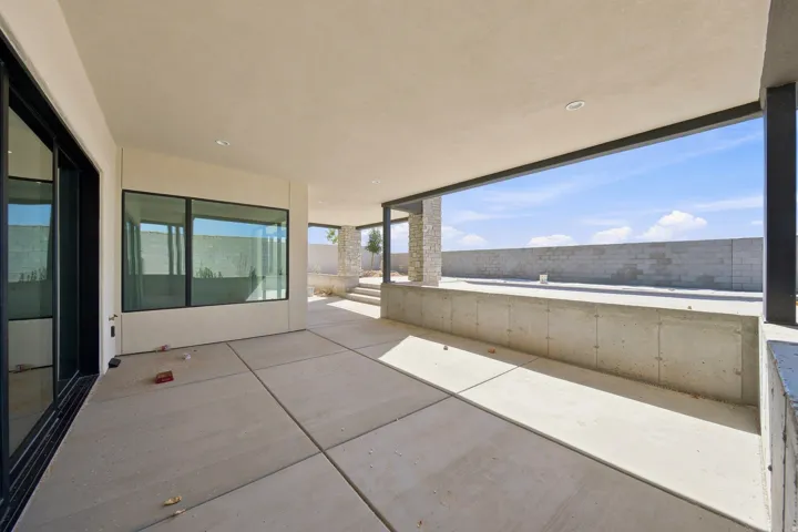 Expansive covered patio with concrete flooring, recessed lighting, and a stone-clad support column