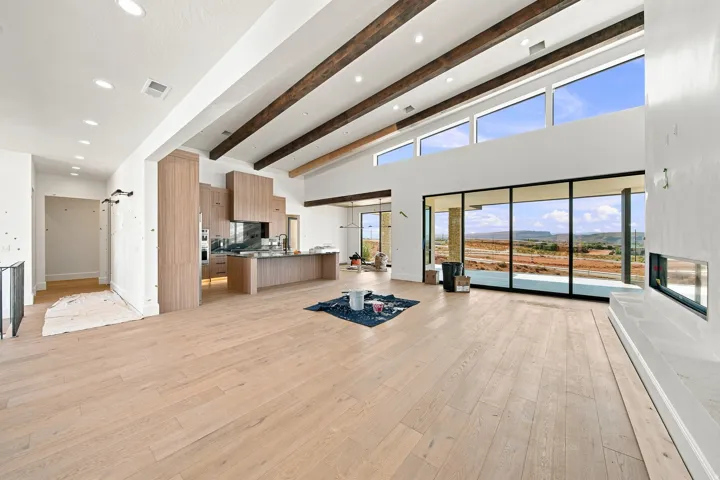 Open-concept living space with soaring wood beam ceilings, recessed lighting, and expansive glass sliding doors framing panoramic landscape vistas