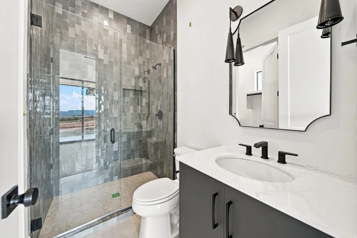 Full bathroom featuring a walk-in shower with tiled walls and a glass enclosure, a vanity with a white countertop and dark cabinetry, and matte black fixtures