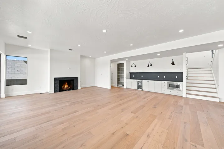 Spacious room featuring wood-finish flooring, a built-in fireplace with a dark stone surround, recessed lighting, and a built-in wet bar with a beverage cooler and microwave