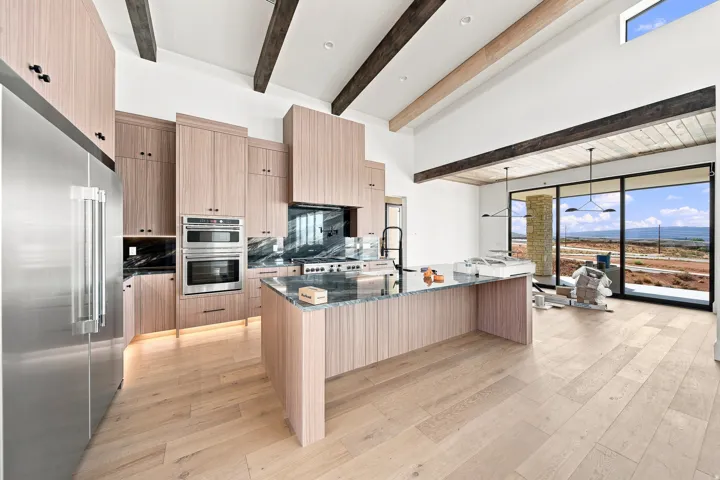 Spacious kitchen featuring light wood-finish cabinetry, a large kitchen island with a stone countertop, integrated stainless steel appliances, and wood-finish flooring