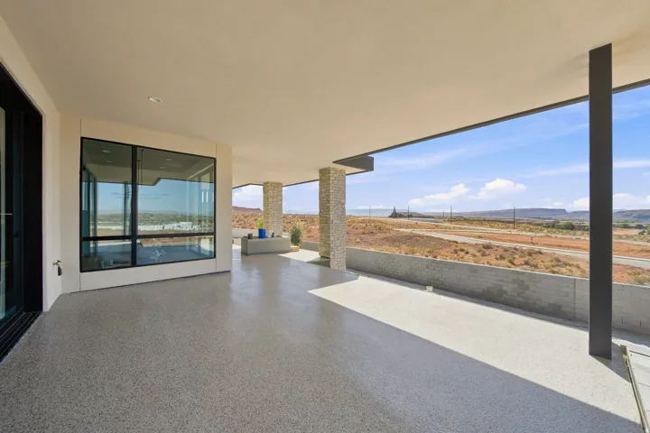 Expansive covered patio with speckled concrete flooring, recessed lighting, and stone-clad pillars