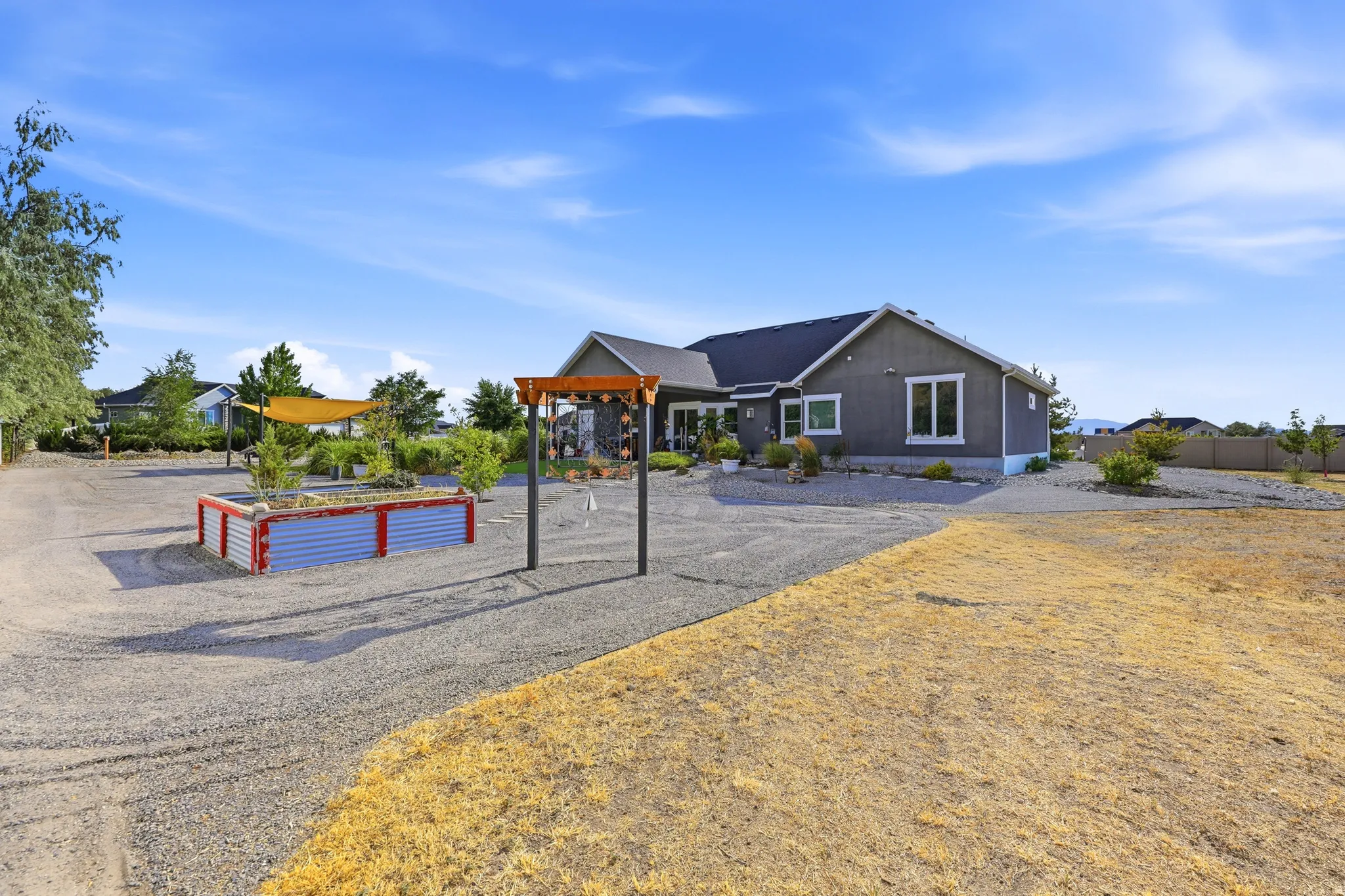 Spacious backyard featuring a large gravel area, raised garden beds with corrugated metal siding, and a wooden pergola structure