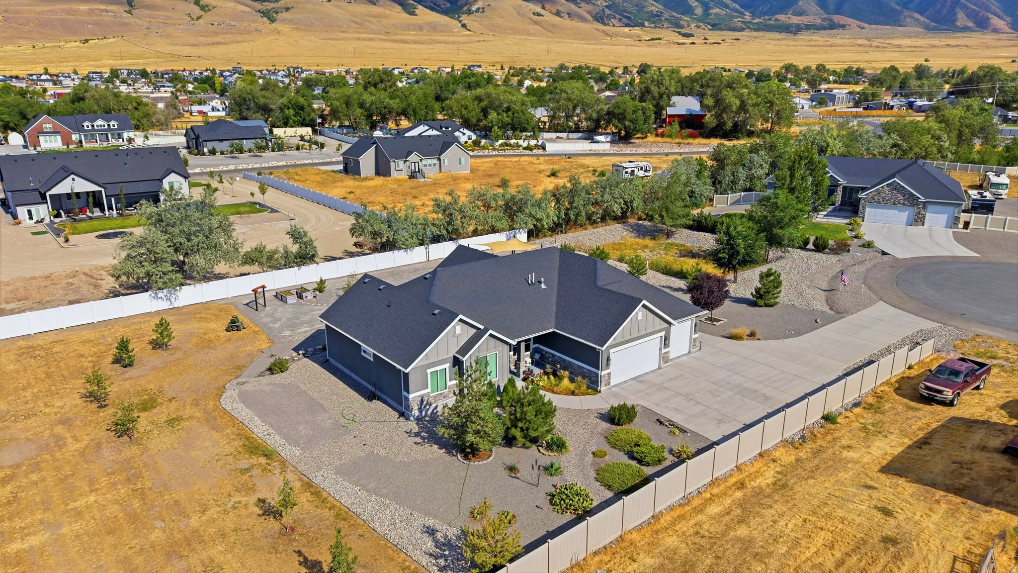 Single-story residence featuring a gray exterior with stone accents, a dark shingle roof, an attached two-car garage, an additional single-car garage, and a landscaped front yard with decorative rock and plantings