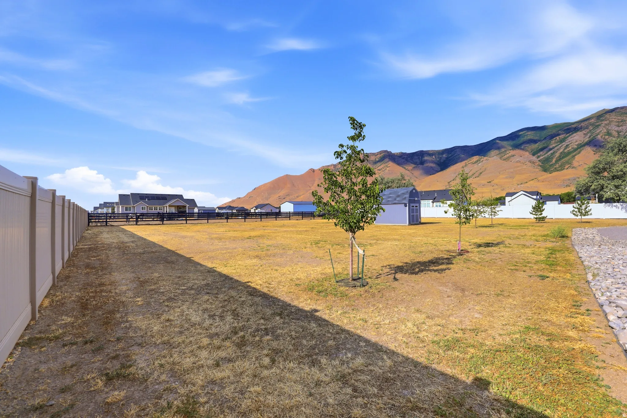 Expansive outdoor space featuring a light-toned vinyl privacy fence, a dark wood-toned fence line, and a distinct mountain backdrop