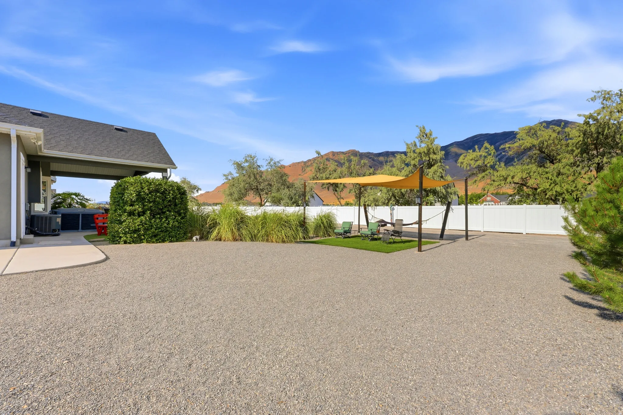 Expansive gravel yard featuring a covered patio, a defined seating area with artificial turf, and a privacy fence
