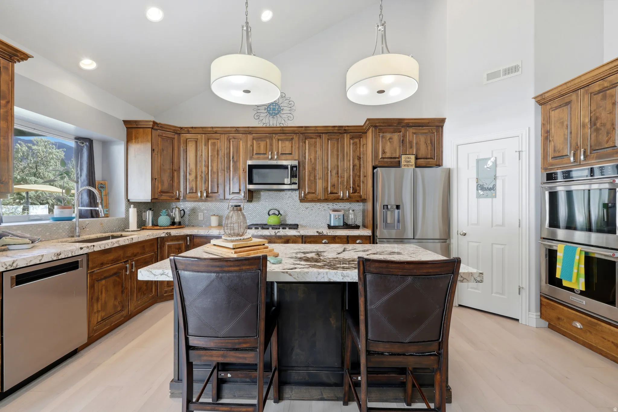 Kitchen featuring vaulted ceilings, wood-finish cabinetry, stainless steel appliances, and a central island with a stone countertop