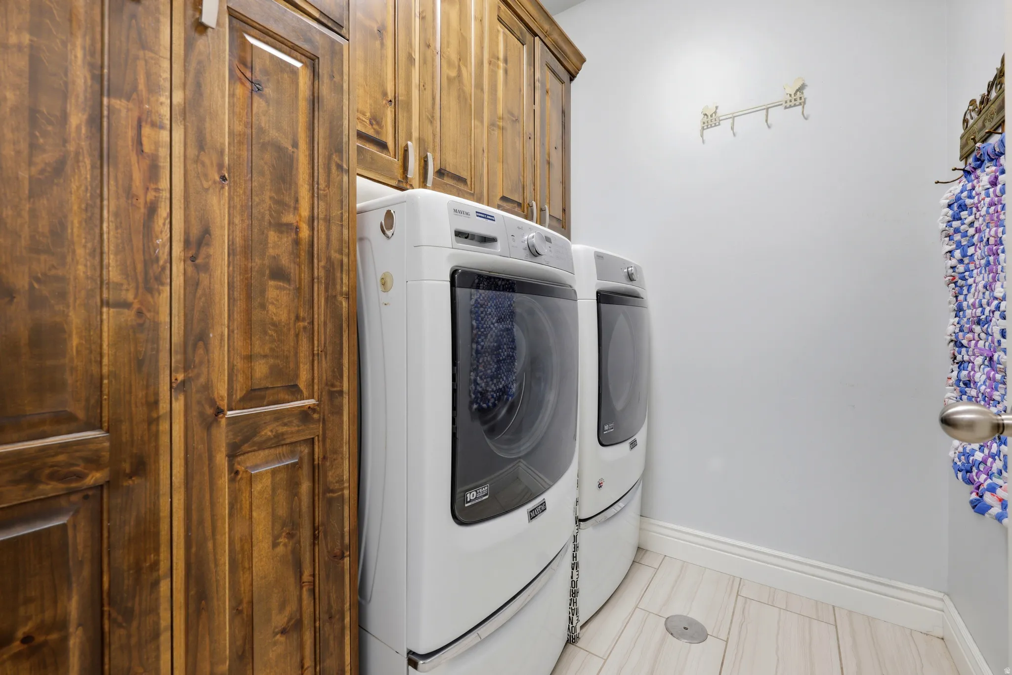 Laundry area featuring extensive wood cabinetry, light-toned wall paint, and light-colored tile flooring