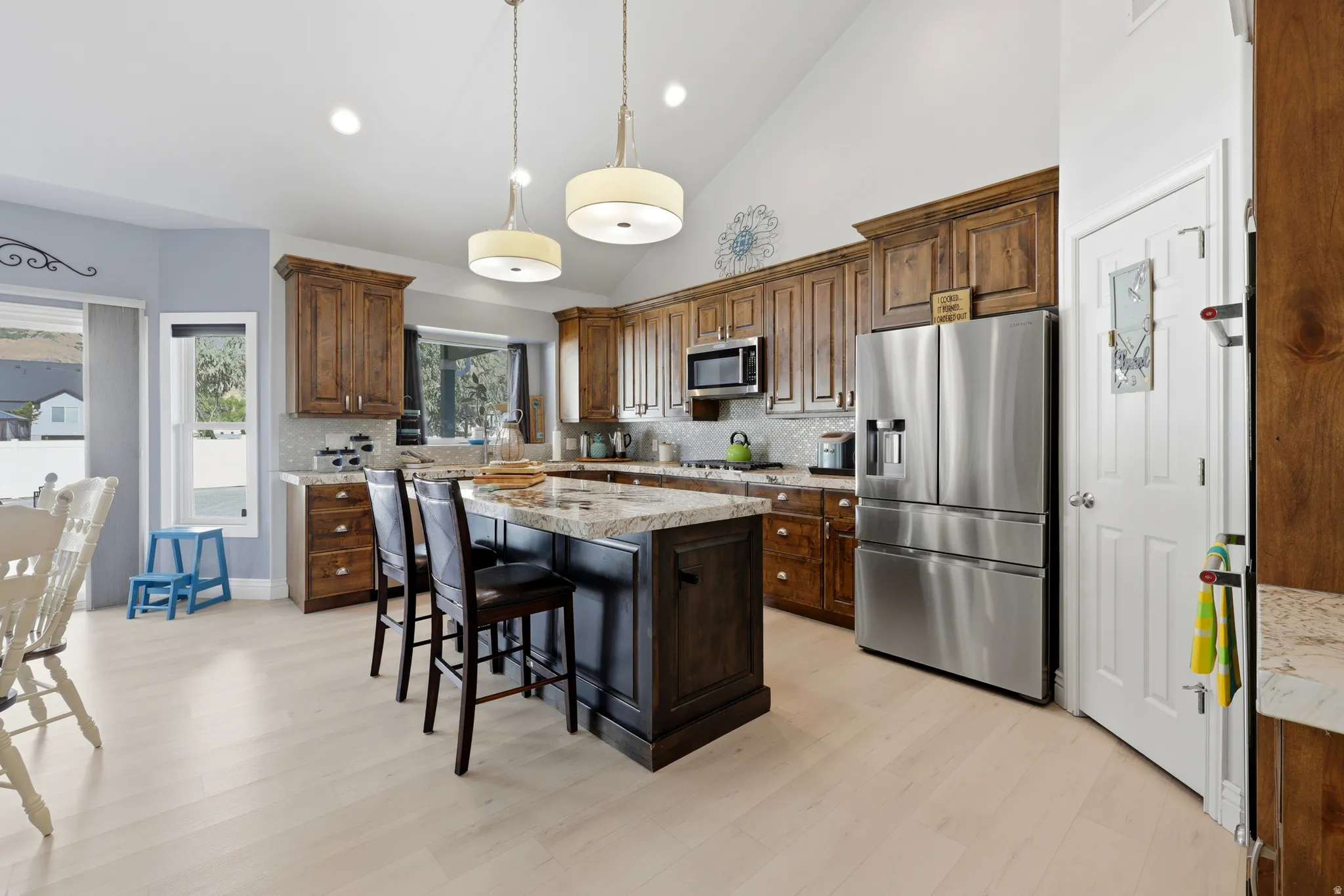 Spacious kitchen featuring an island with stone countertops, stainless steel appliances, wood-finish flooring, and vaulted ceilings