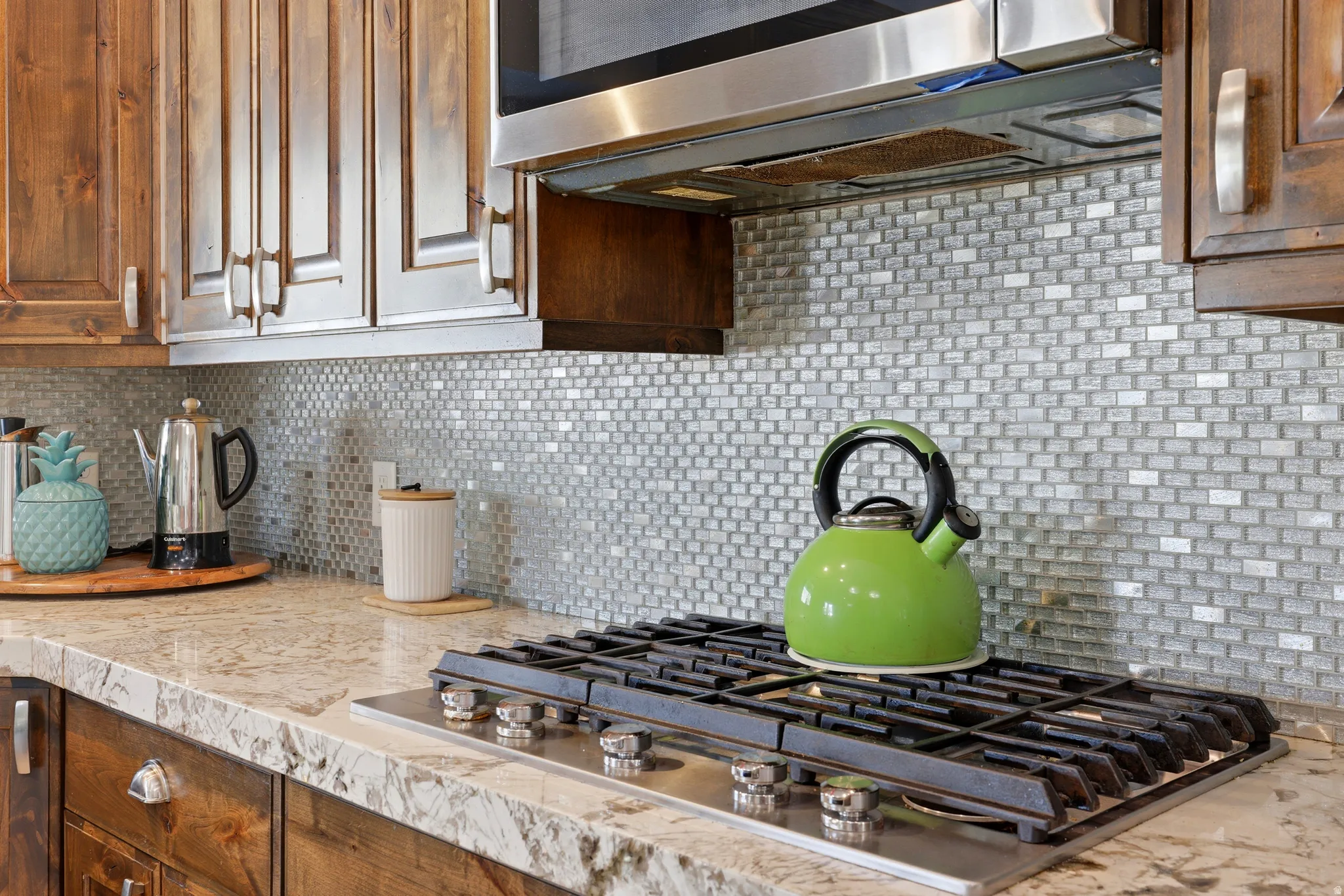 Kitchen featuring a stainless steel gas cooktop, stone countertops, wood cabinetry, and a mosaic tile backsplash