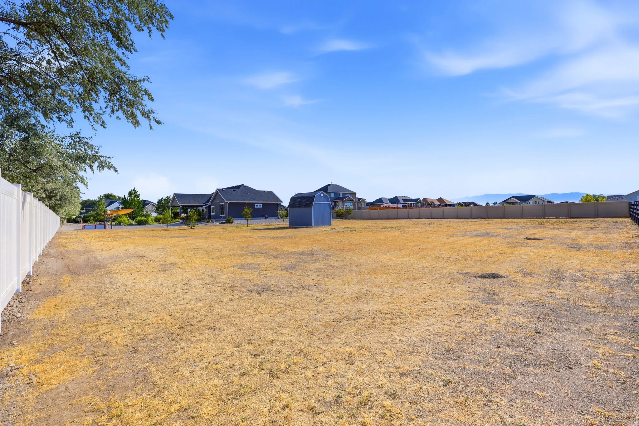 Expansive open lot featuring a white privacy fence, mountain backdrop, and a detached storage shed