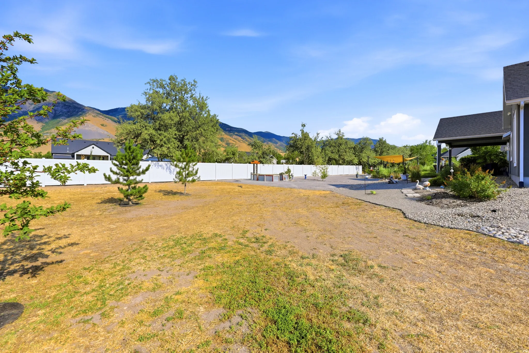 Expansive backyard featuring a white privacy fence, gravel hardscaping, and a mature tree-lined perimeter