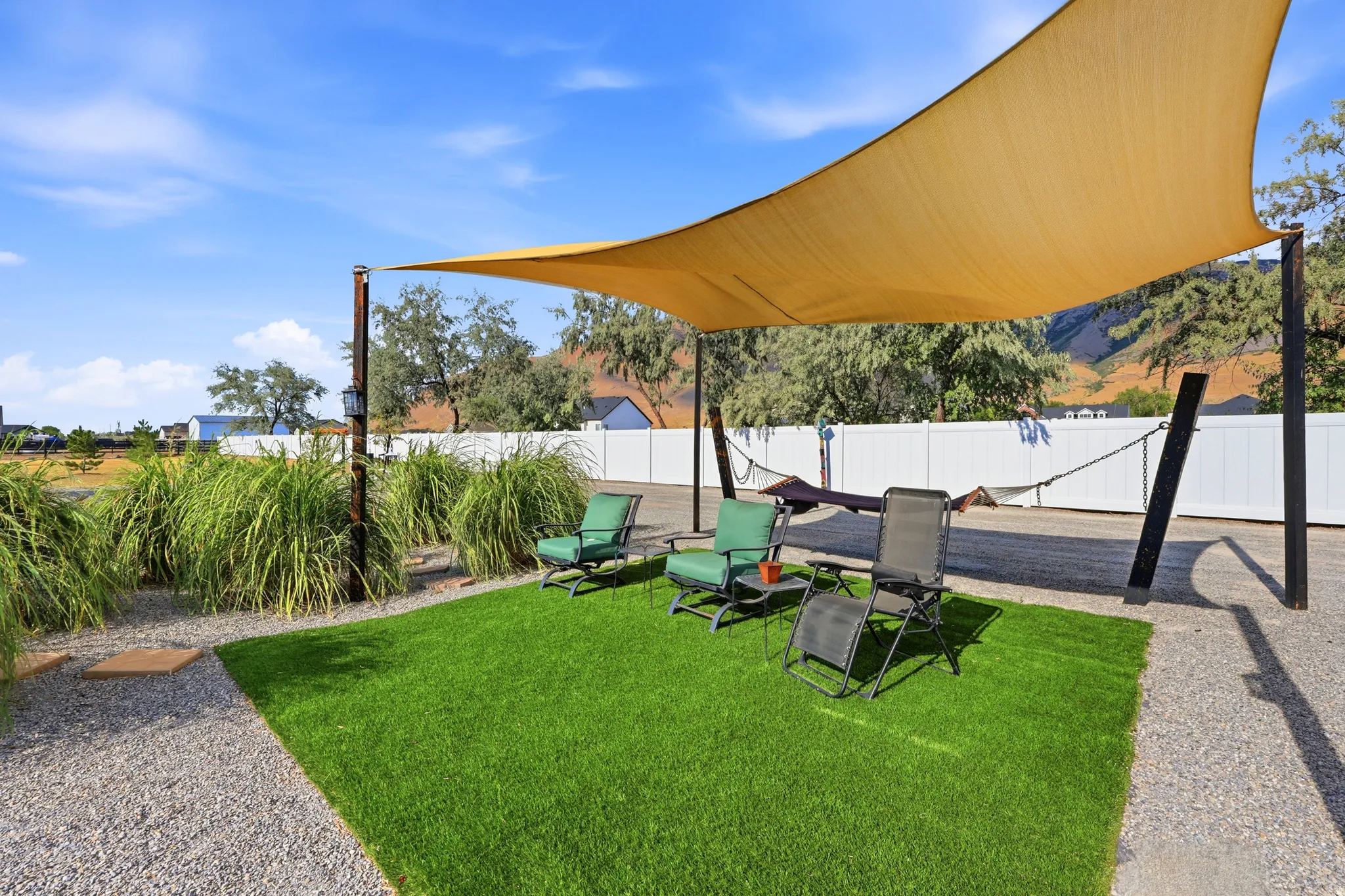 Outdoor living space featuring a large shade sail, artificial turf patio, and gravel pathways