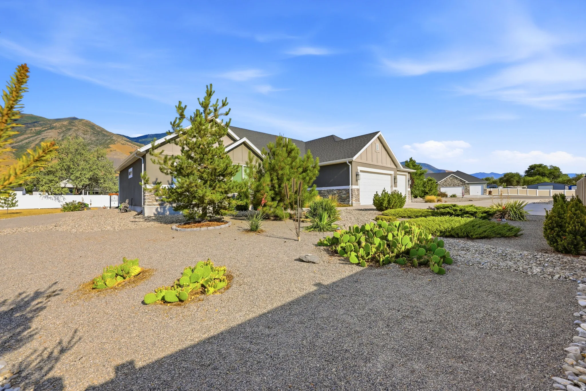 Contemporary residence featuring a two-car garage, stone and siding exterior, xeriscaped front yard with diverse plantings, and a mountain backdrop
