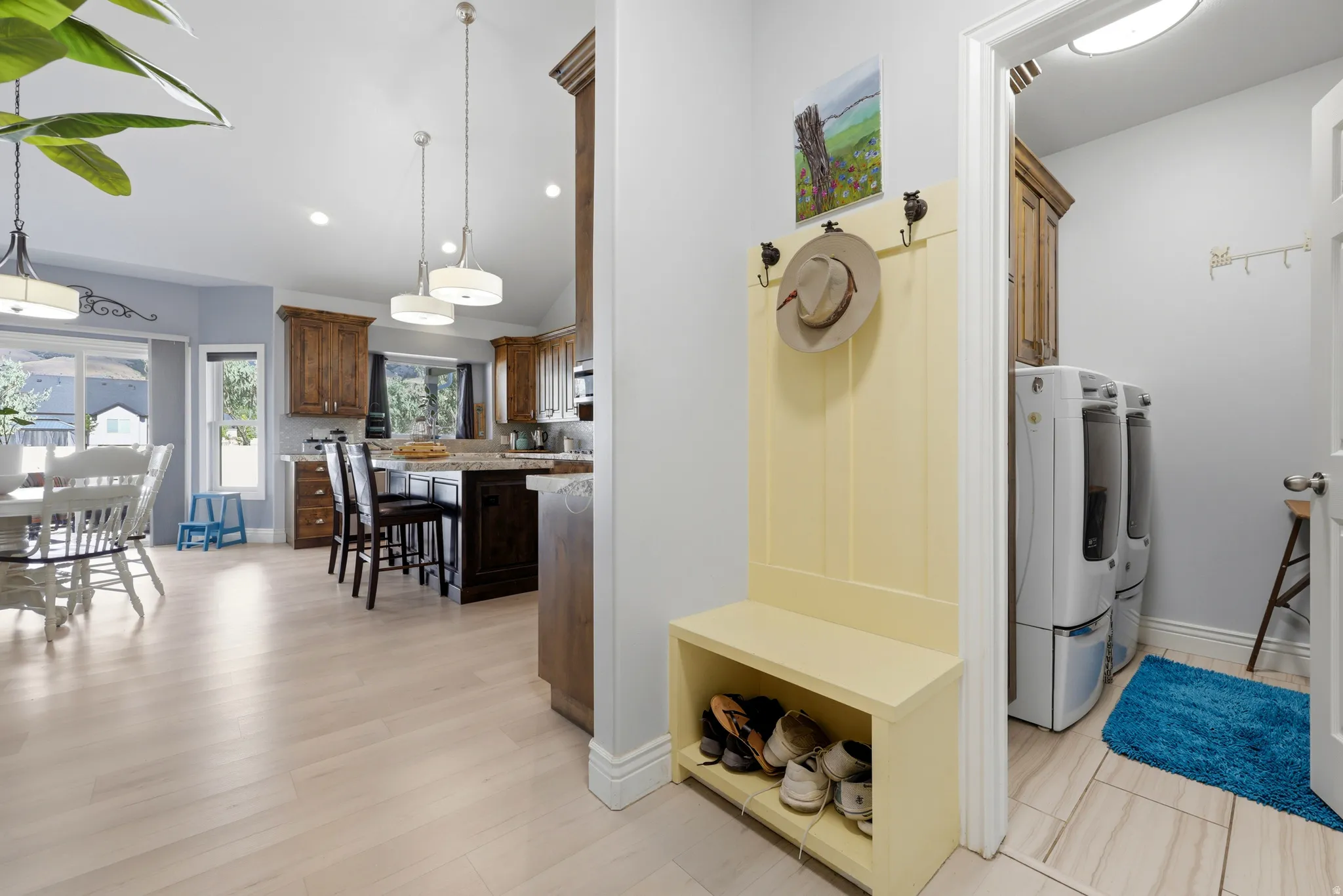 Light wood-finish flooring extending into an open-concept kitchen with recessed lighting and pendant fixtures