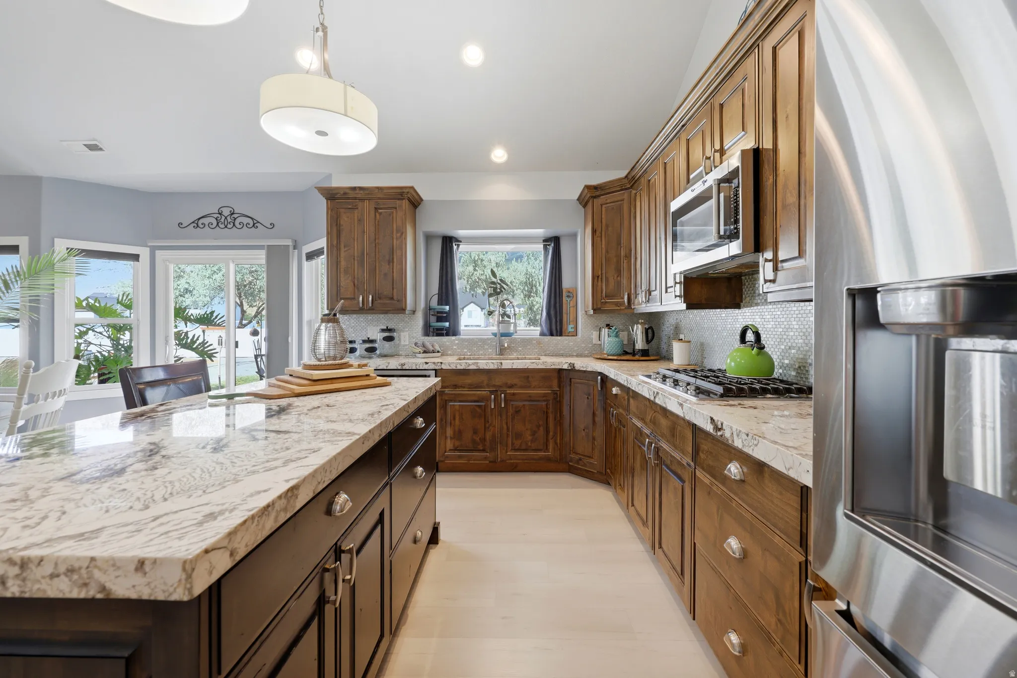Kitchen featuring wood-finish cabinetry, stainless steel appliances, a large center island with a light-toned stone countertop, and a tile backsplash