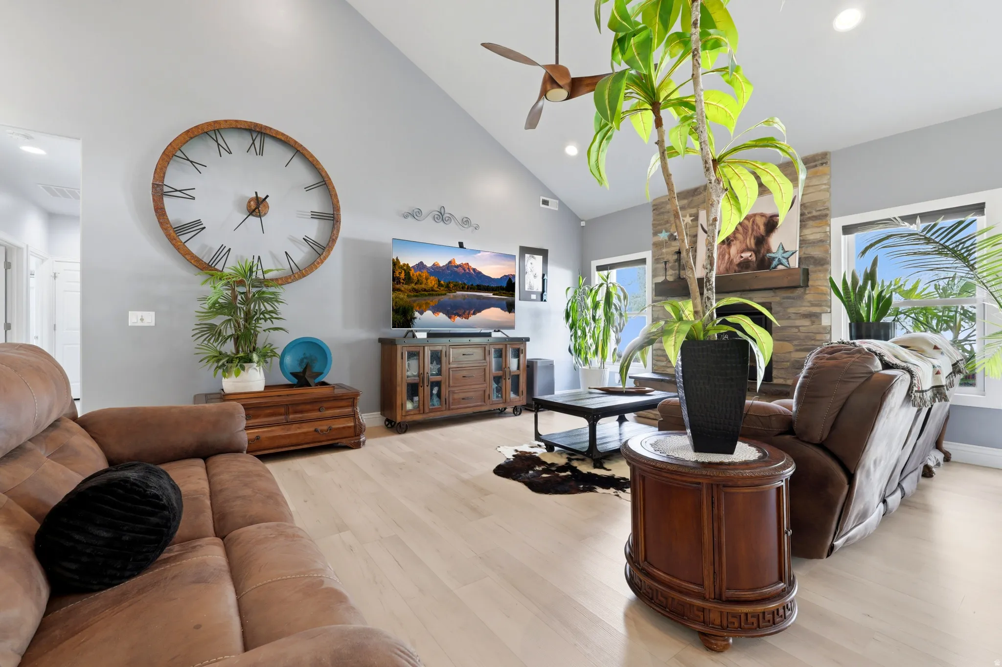 Spacious living area featuring light wood-finish flooring, a vaulted ceiling, and a stacked stone fireplace with a wood mantel