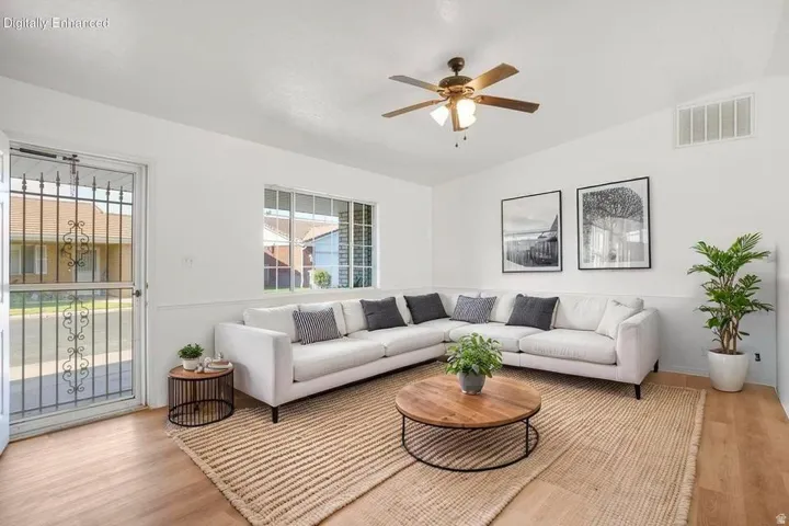 Bright living area featuring wood-finish flooring, white walls with wainscoting, and a ceiling fan with integrated lighting