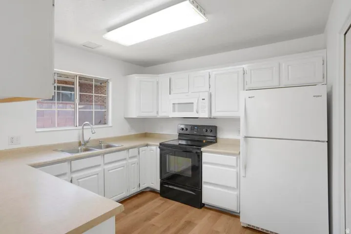 Kitchen featuring white cabinetry, light-toned countertops, a stainless steel double basin sink with a gooseneck faucet, black range, and wood-finish flooring