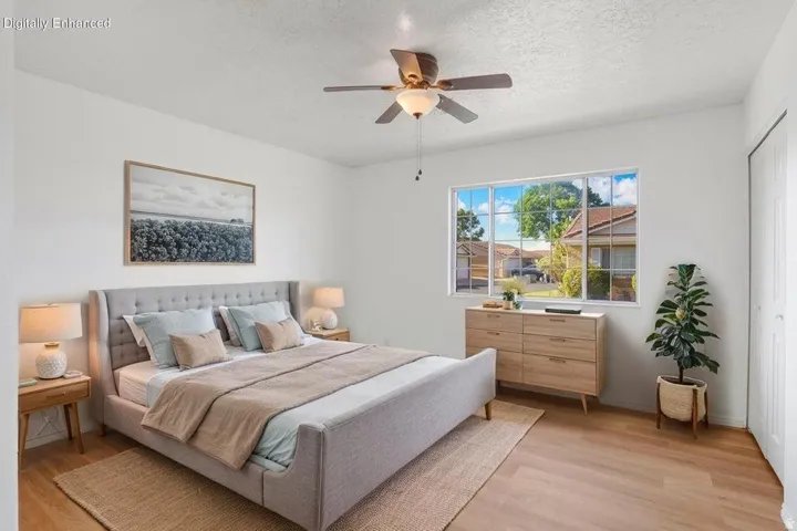 Bright room featuring wood-finish flooring, a ceiling fan with integrated lighting, a spacious window, and a built-in closet with white bifold doors