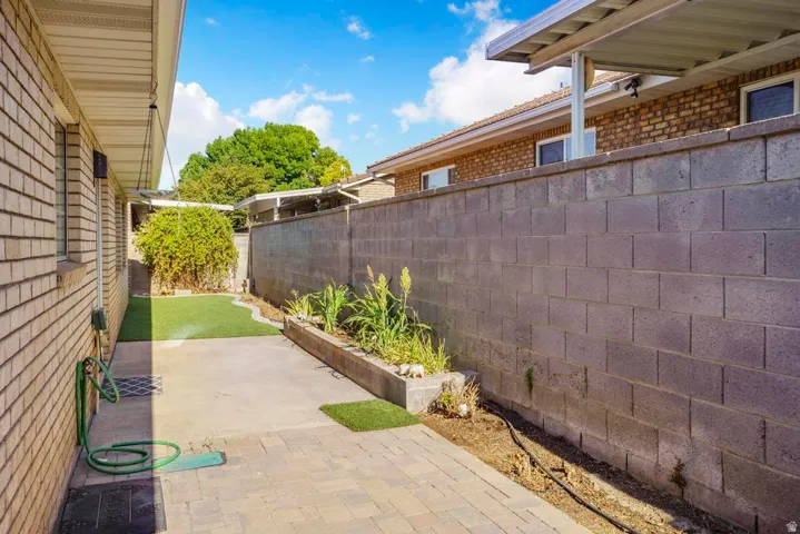 Private side yard featuring a concrete block wall, paver patio, and synthetic turf sections