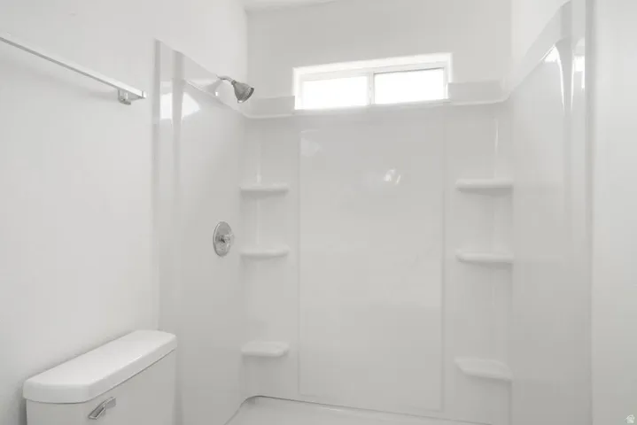 White shower enclosure with integrated shelving, chrome shower head, and a transom window