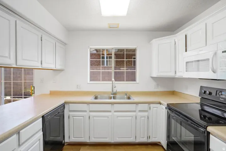 U-shaped kitchen featuring white cabinetry, light-toned countertops, and a dual basin stainless steel sink