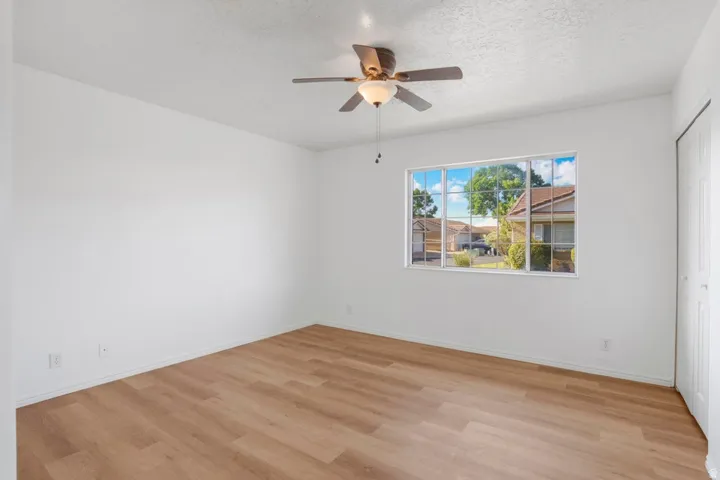 Room featuring wood-finish flooring, a ceiling fan with integrated lighting, and a large multi-pane window