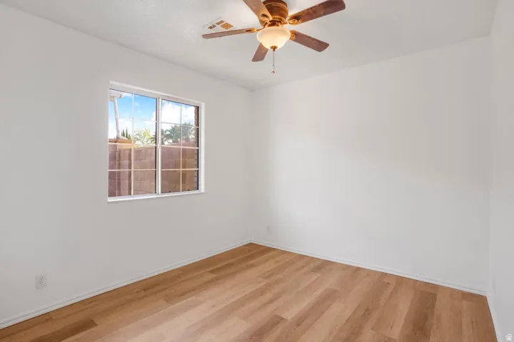 Room featuring wood-finish flooring, white walls, and a ceiling fan with integrated lighting