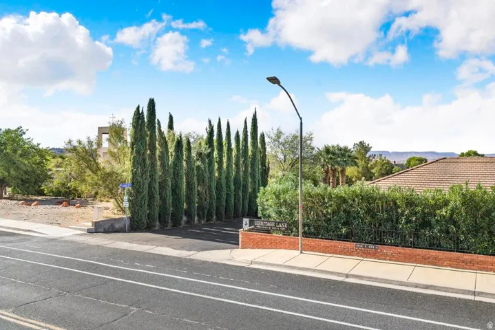 Gated community entrance featuring a brick wall, mature cypress trees, and a visible street sign