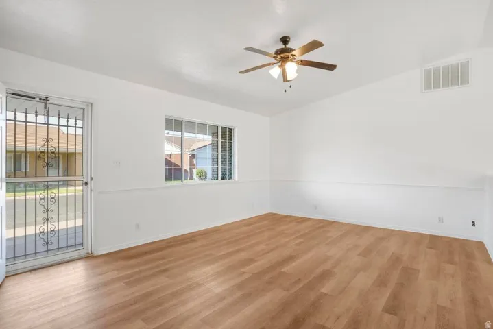 Spacious room featuring wood-finish flooring, white walls, and a ceiling fan with integrated lighting
