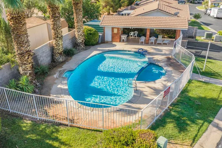 Irregularly shaped pool with integrated hot tub, surrounded by concrete decking and a white metal fence
