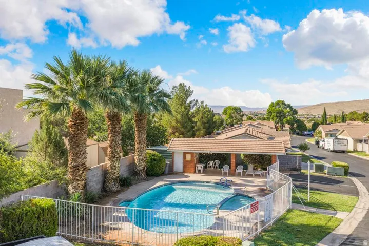 Fenced outdoor swimming pool with an integrated spa, surrounded by a concrete deck and a covered patio area