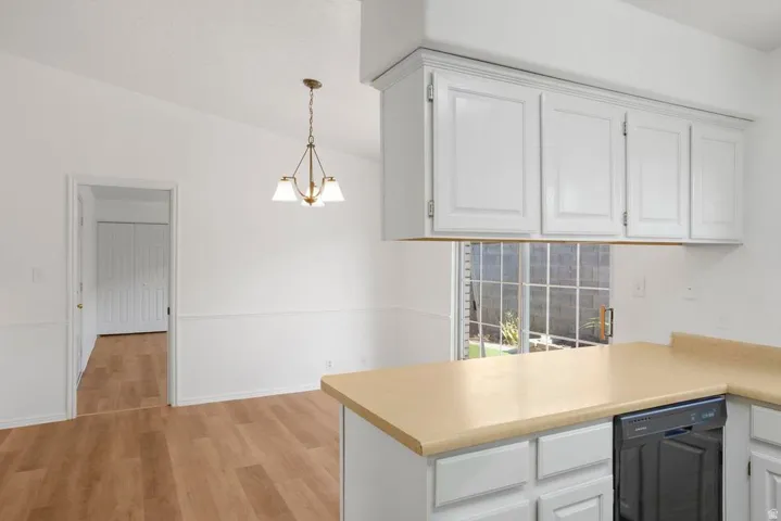 Kitchen and dining area featuring wood-finish flooring, white cabinetry, a built-in dishwasher, and a brass-tone chandelier