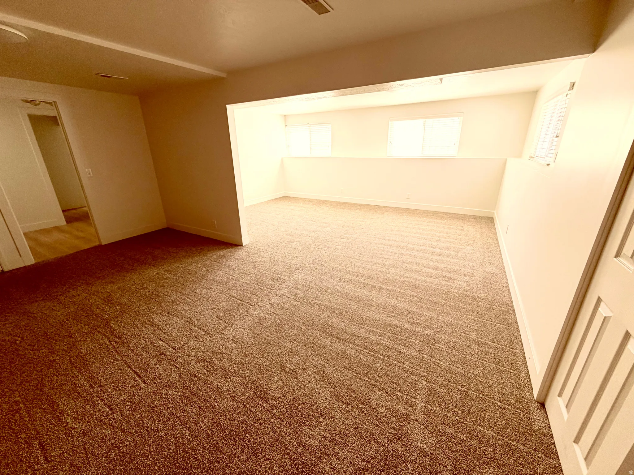 Spacious room featuring neutral carpeting, white painted walls, and an integrated transom opening to a secondary area with windows