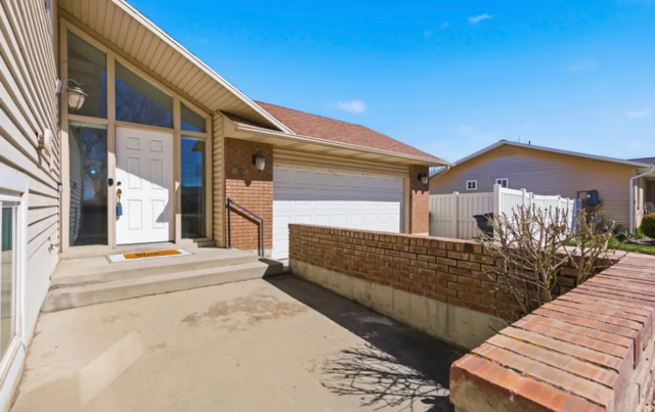 Inviting entryway featuring a white paneled door with sidelights and an angled transom window, concrete steps, and a garage with a brick facade