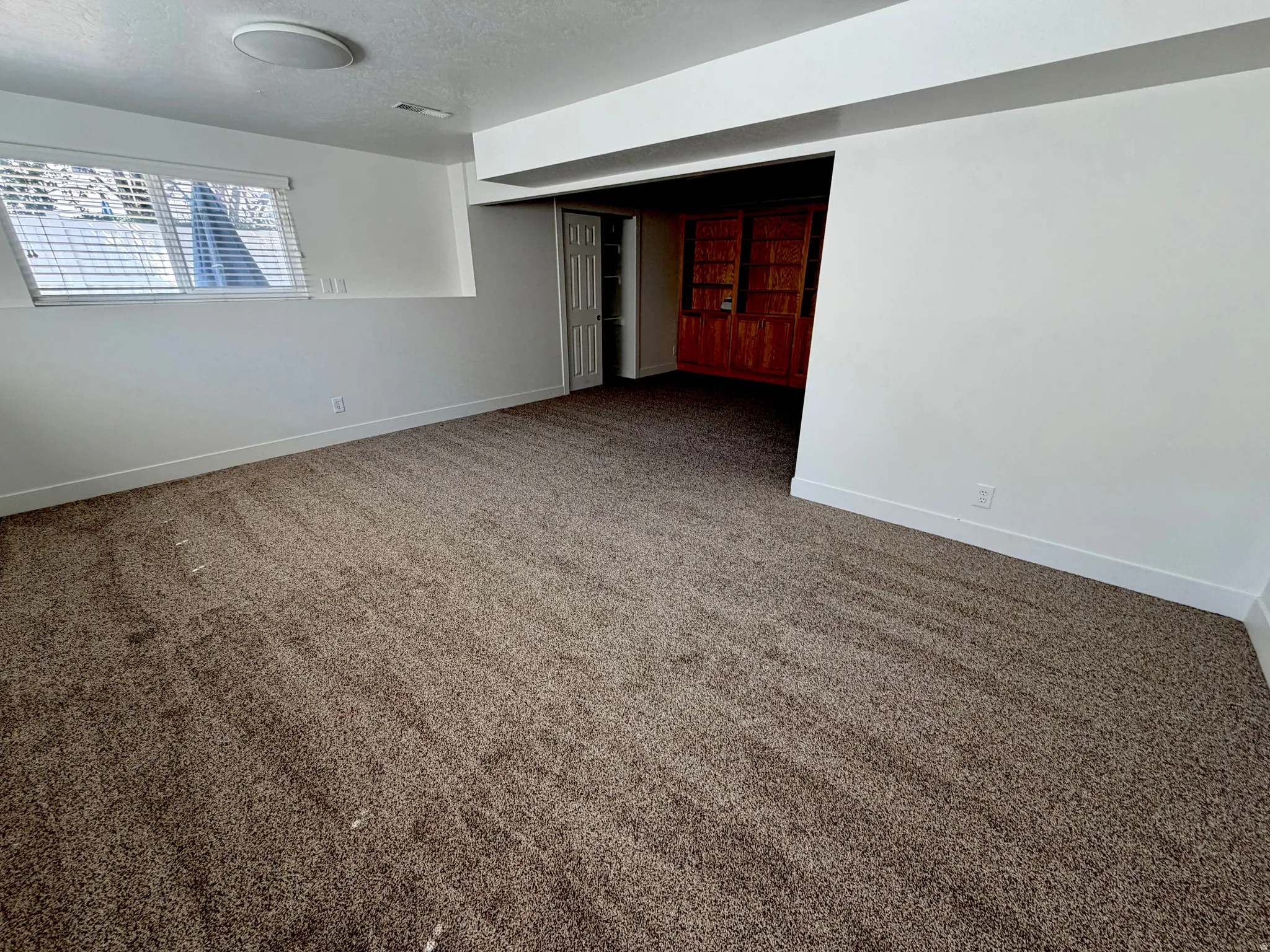 Spacious room featuring neutral carpeting, a white ceiling with recessed lighting, and a window with blinds