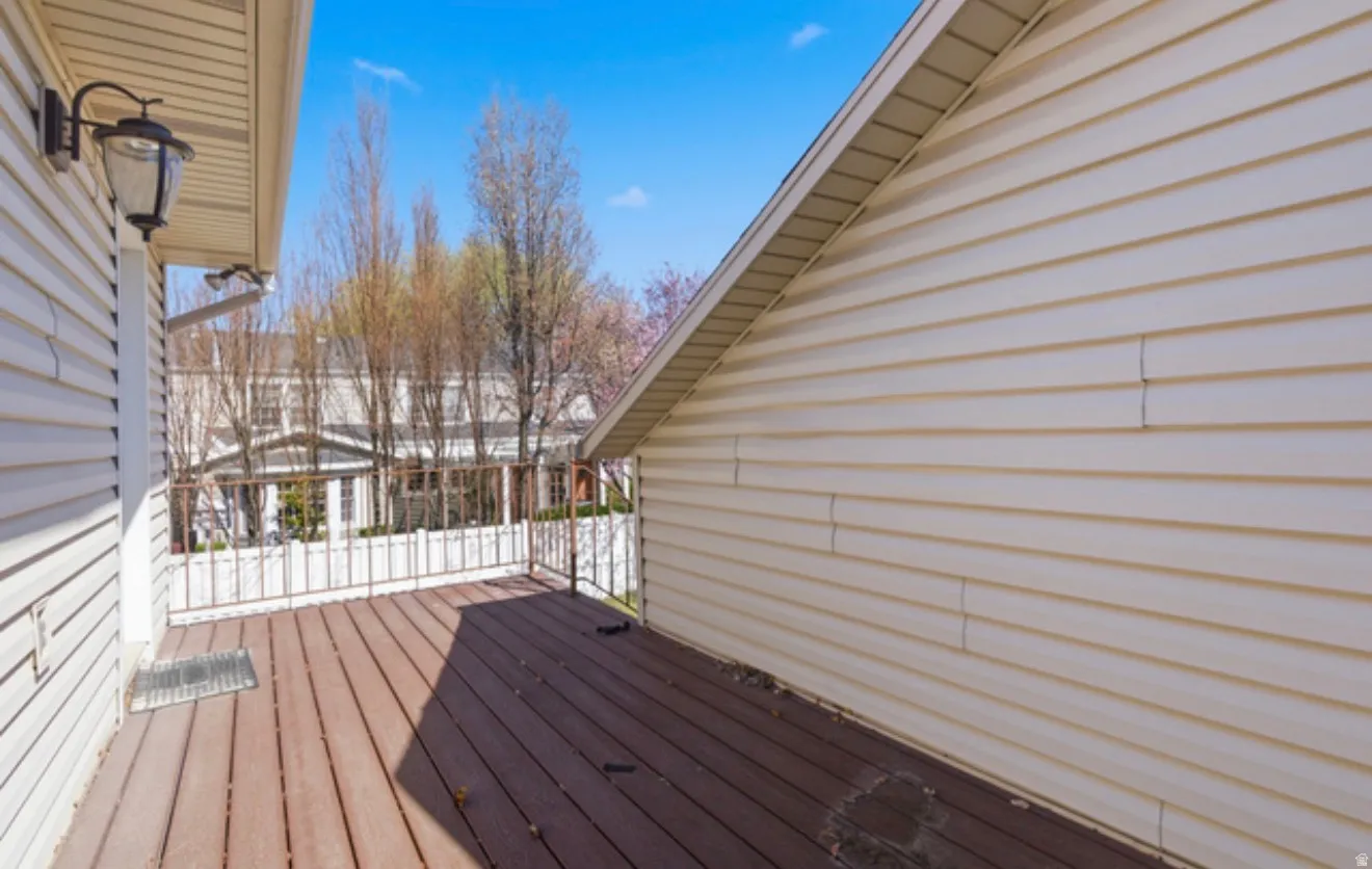 Outdoor deck featuring composite decking, white siding, white railing, and an exterior wall light fixture