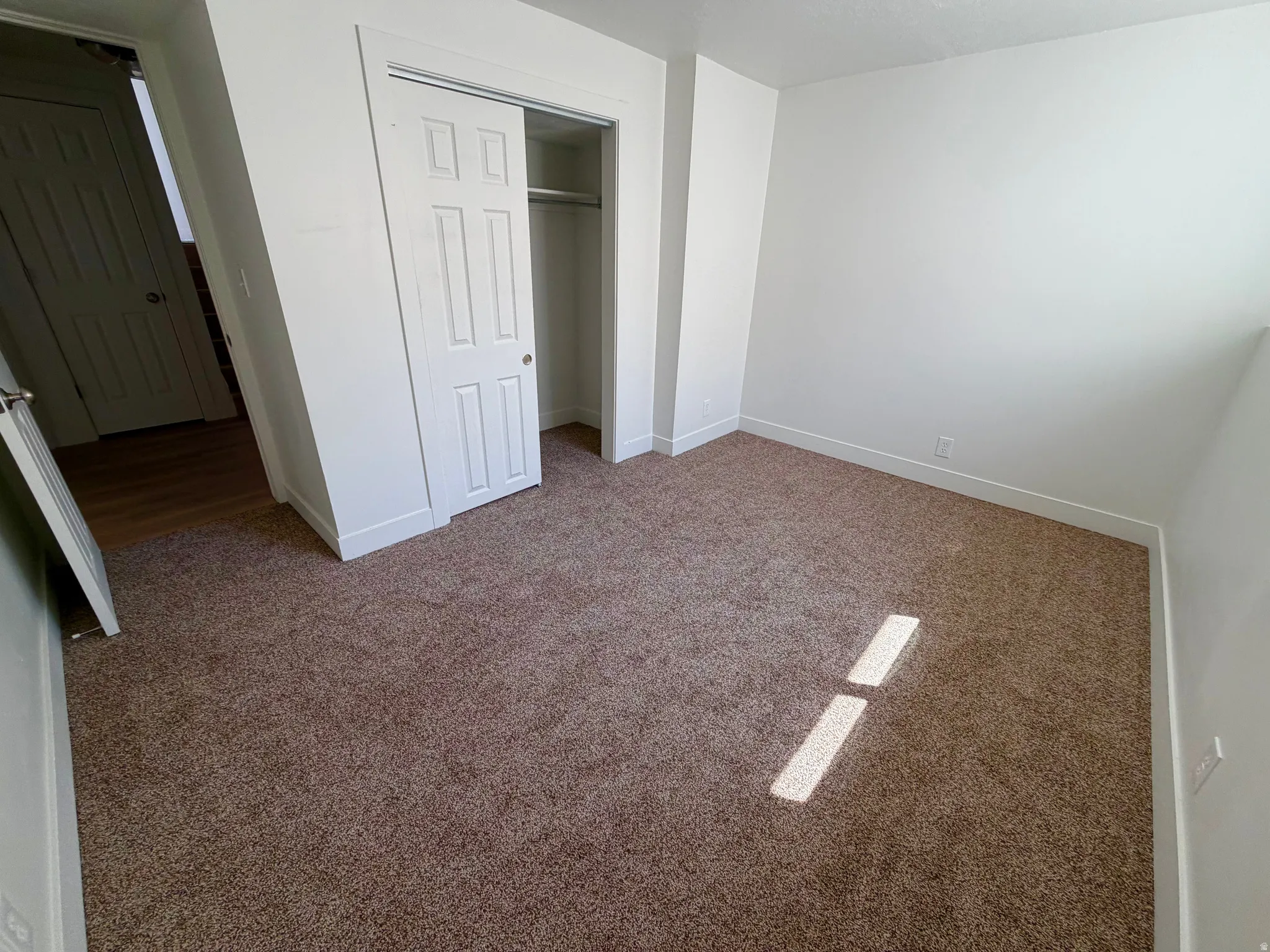 Carpeted room featuring white walls, white trim, and a bi-fold closet with a six-panel door