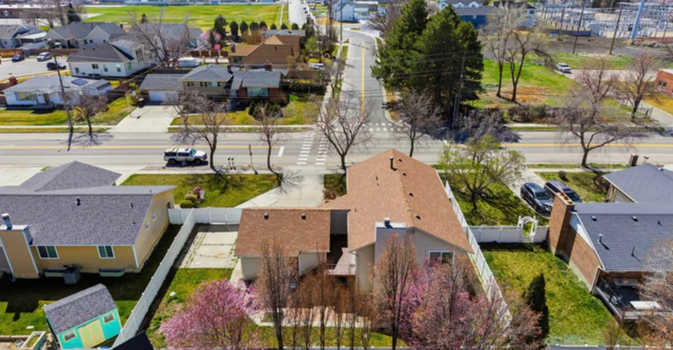 Aerial view of a residential property featuring a brown shingle roof, a fenced backyard with green lawn, and mature trees