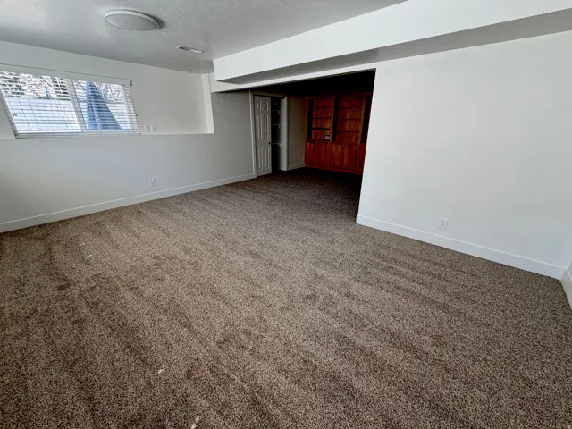 Spacious room featuring neutral carpeting, a white ceiling with recessed lighting, and a window with blinds