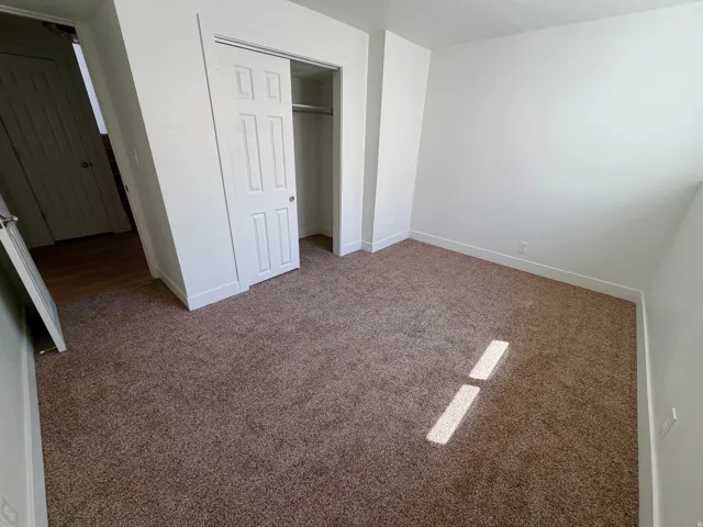Carpeted room featuring white walls, white trim, and a bi-fold closet with a six-panel door