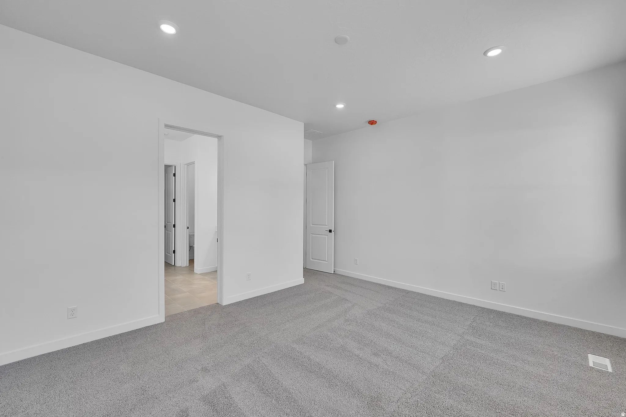Spacious room featuring neutral carpeting, recessed lighting, white walls, and a doorway leading to an additional space