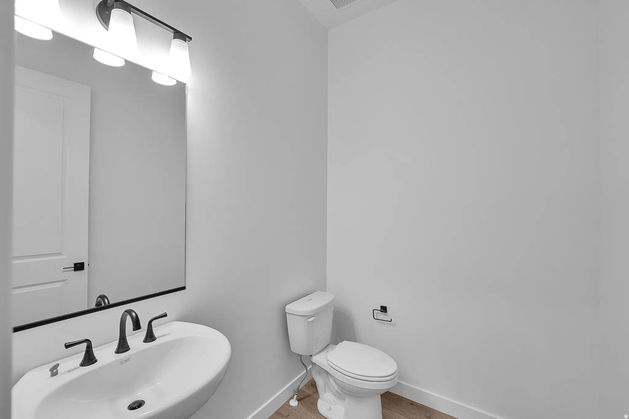 Modern powder room featuring a wall-mounted sink with matte black faucet, a rectangular mirror, and a three-light vanity fixture