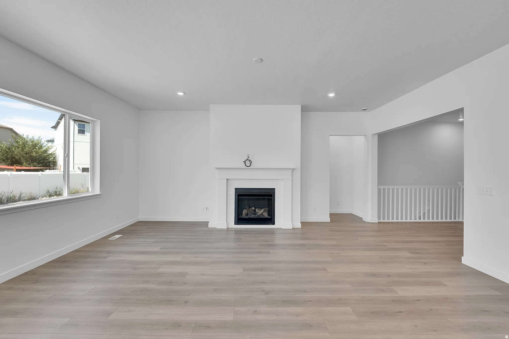 Spacious living area featuring a prominent white fireplace with a mantel, wood-finish flooring, recessed lighting, and large windows