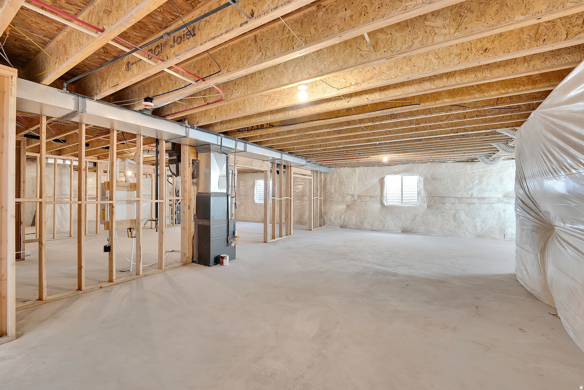 Expansive unfinished basement featuring visible wood joists, structural framing, concrete flooring, and an insulated wall with a window