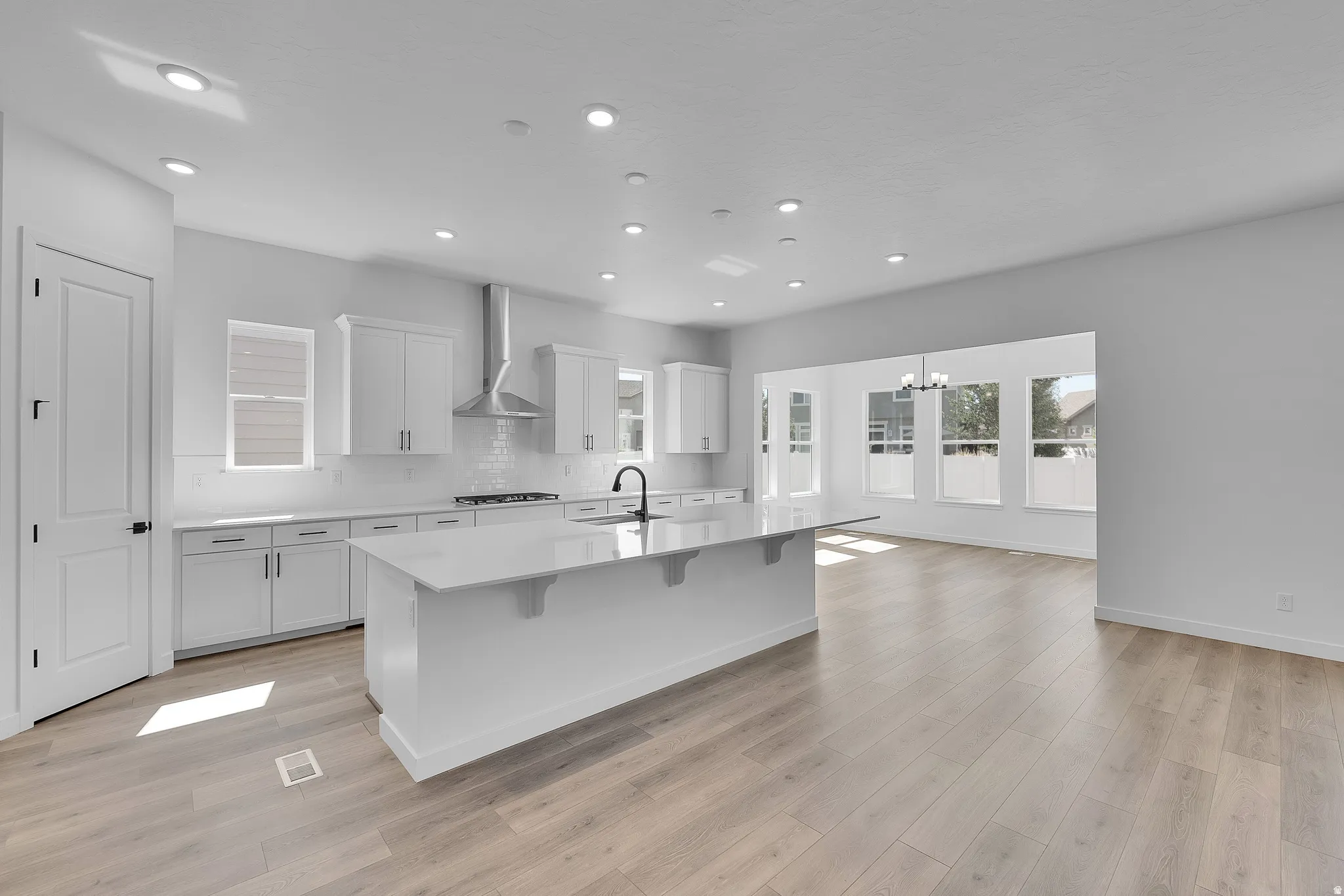 Bright kitchen featuring white cabinetry, a large center island with a stone-finish countertop, a subway tile backsplash, and wood-finish flooring