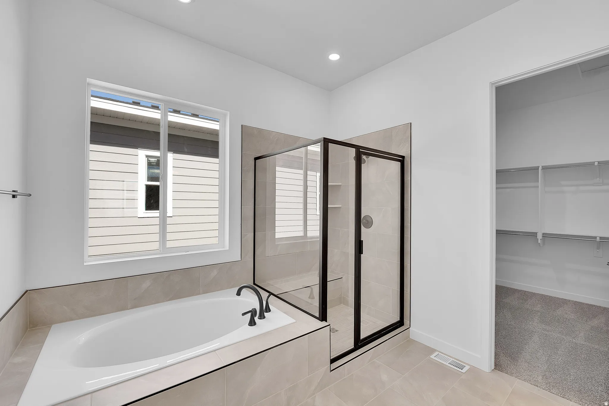 Contemporary bathroom featuring a built-in soaking tub with dark bronze fixtures, a glass-enclosed shower with a tiled surround, recessed lighting, and a window with a white frame