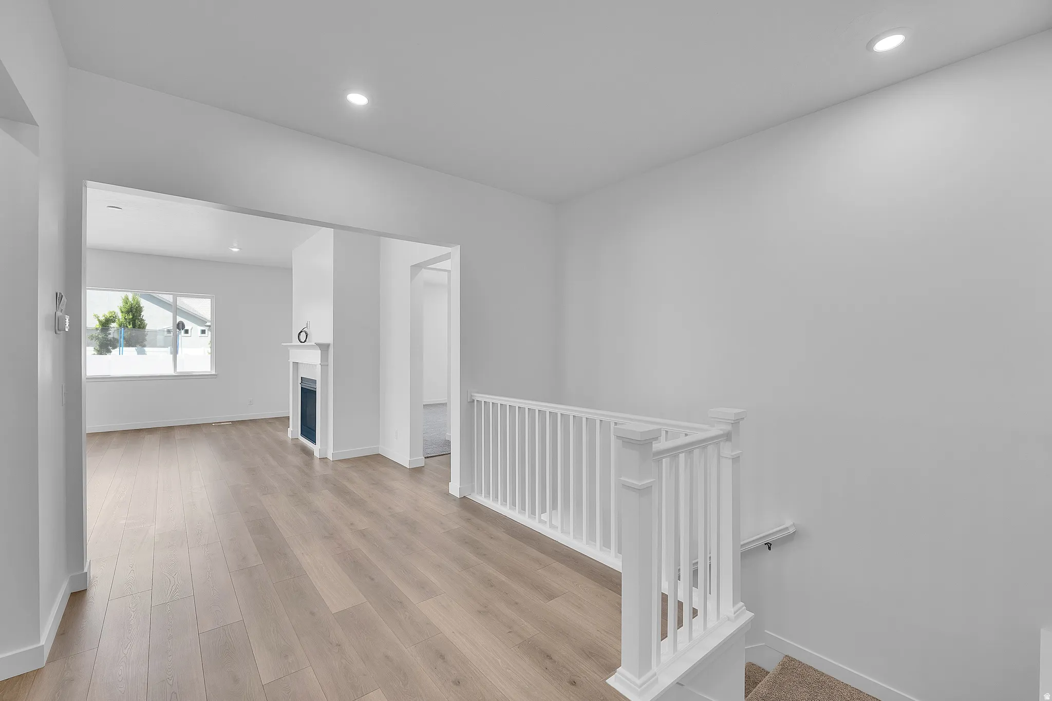 Bright interior featuring wood-finish flooring, a white staircase with a classic balustrade, and recessed lighting