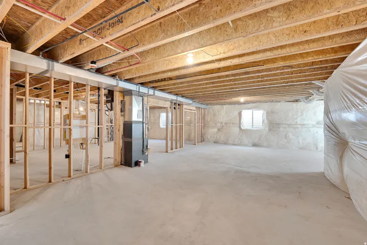 Expansive unfinished basement featuring visible wood joists, structural framing, concrete flooring, and an insulated wall with a window